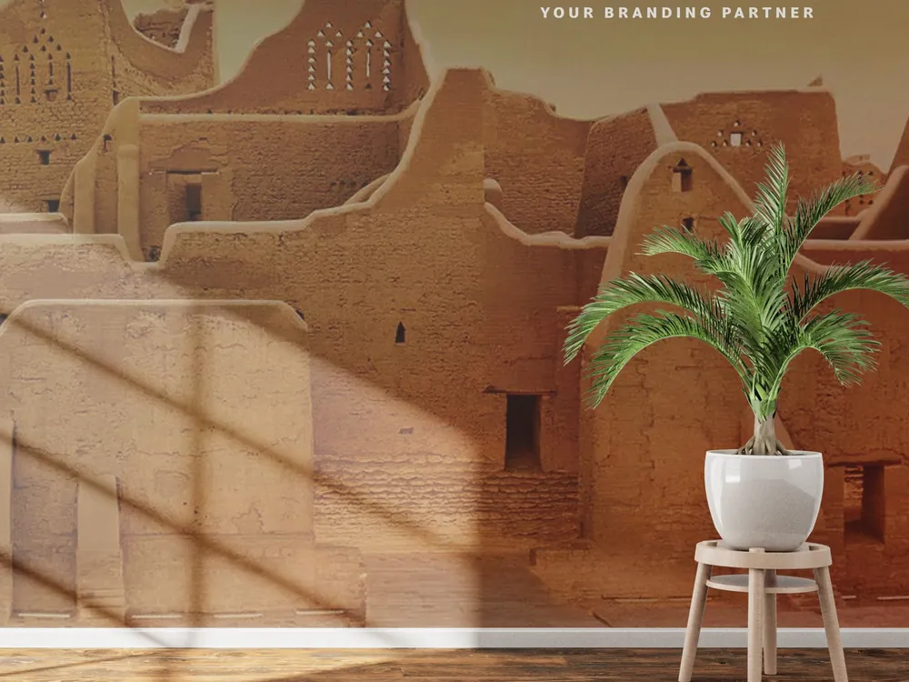 Printed wall mural of traditional mud-brick architecture behind a potted palm